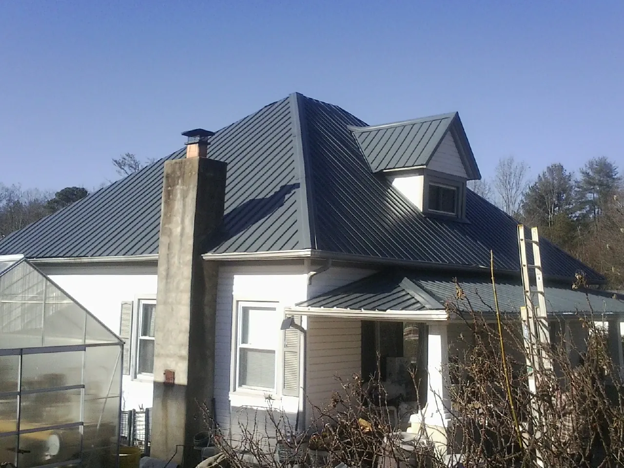 Dark blue standing seam metal roof on a white farmhouse with dormer — Slate & Tile Roof Repair by Roofing Brothers in Haysville
