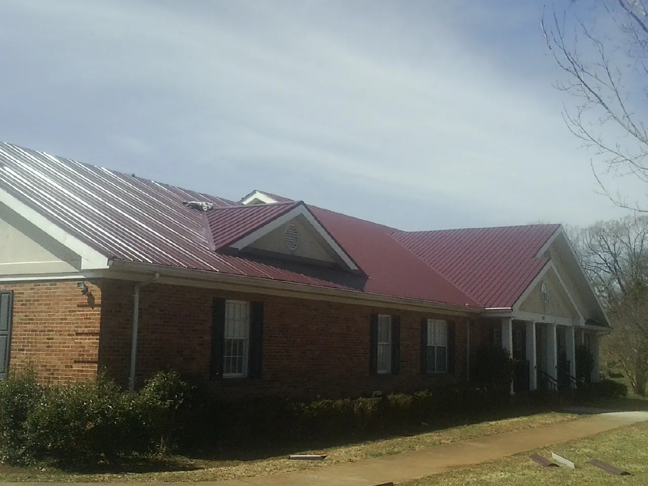 Red metal roof with gabled entries on a long brick building, from a Hail Damage Roof Repair job in Haysville