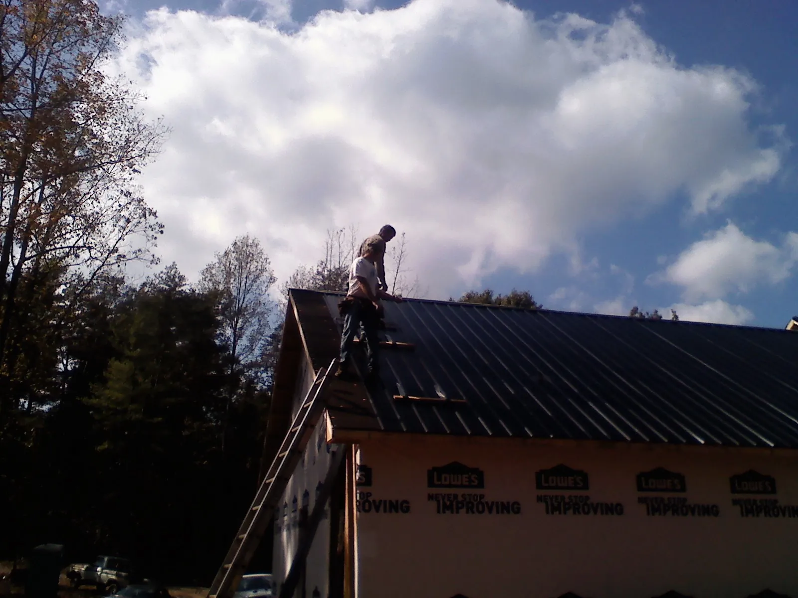 Roofer fastening dark metal panels high against a cloudy sky, from a Roof Inspection job in Haysville