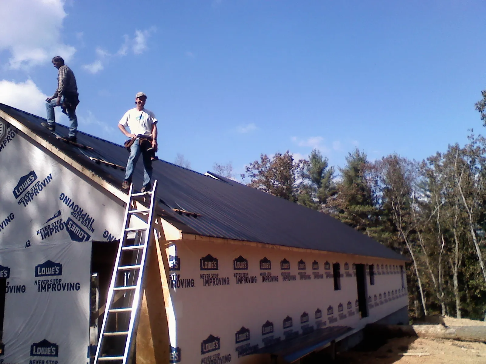 Two roofers standing on a long dark metal roof over a wrapped building in Haysville