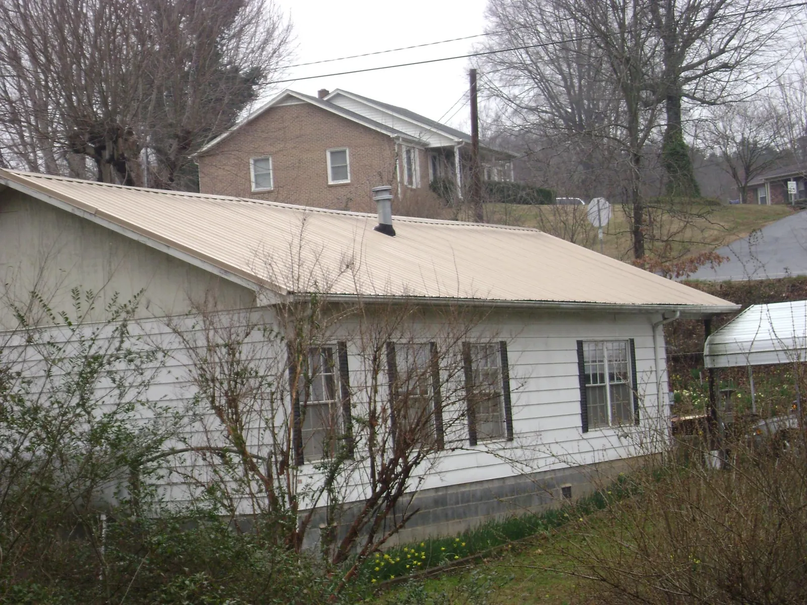 Tan metal roof on a white sided house set into a hillside — Commercial Roofing by Roofing Brothers in Haysville